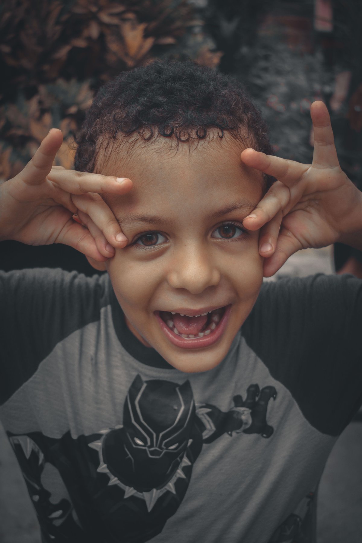 A young boy with curly hair wearing a Black Panther t-shirt, making a silly face